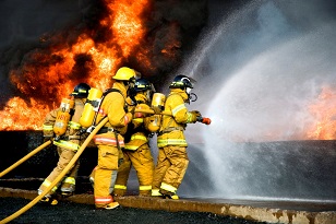 Firefighters in full gear holding hose and battling large flames