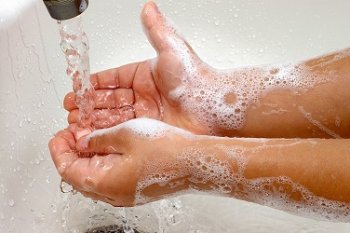 A child's hands soapy and under running water from a faucet
