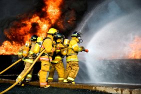 Bomberos en trajes de protección completa luchando llamas y rociando agua con mangueras grandes